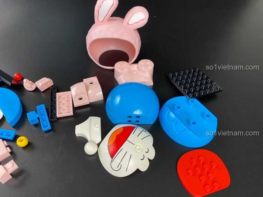 Các chi tiết để lắp ráp mô hình Keeppley Doraemon KUPPY Thỏ Hồng, gồm các mảnh màu hồng, xanh, trắng.