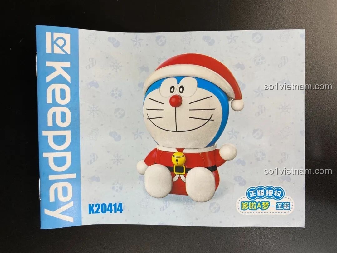 Mở hộp bộ lắp ráp Doraemon Giáng Sinh, bên trong là các mảnh ghép màu đỏ, trắng và xanh.